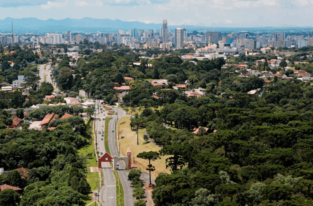 Imagem aérea da cidade de Curitiba, Paraná. Com avenida e árvores.