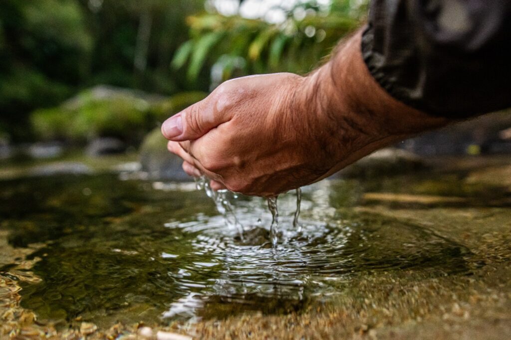 Imagem de uma mão pegando água de um rio.